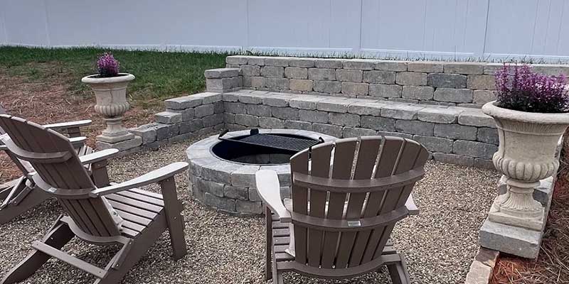 gravel patio with deck chairs and a fire pit surrounded by a leveled retaining wall 
