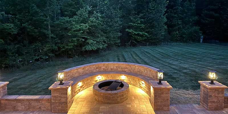 night, wide shot of a stone fire pit built by santos hardscape & tree services illuminated by landscape lighting