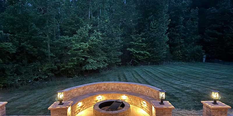 outdoor, stone fire pit surrounded by a retaining wall with hardscape lighting installed<br />